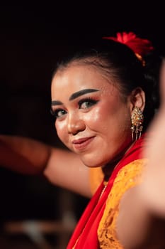 Beautiful face of an Indonesian woman in makeup while dancing a traditional dance in an orange costume during the festival in the night