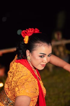 Beautiful face of an Indonesian woman in makeup while dancing a traditional dance in an orange costume during the festival in the night