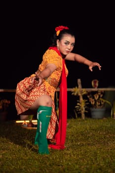 Balinese woman in traditional orange dress dancing with a red scarf while performing dancing in the night