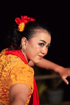 Beautiful face of an Indonesian woman in makeup while dancing a traditional dance in an orange costume during the festival in the night