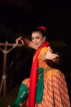 Balinese woman in traditional orange dress dancing with a red scarf while performing dancing in the night