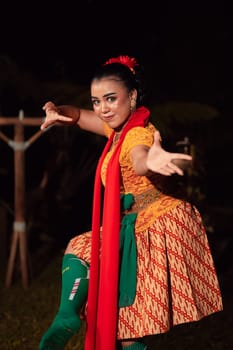 Balinese woman in traditional orange dress dancing with a red scarf while performing dancing in the night