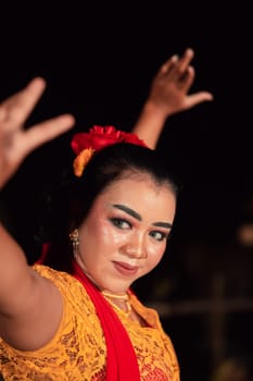 An Asian Traditional dancer in an orange dress with a red scarf and makeup performing at the dance festival in the night