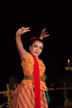 Balinese woman in traditional orange dress dancing with a red scarf while performing dancing in the night
