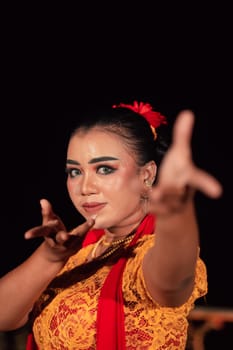 A Balinese woman poses with both her hands in a traditional orange dress and red scarf on her body in the festival