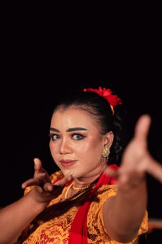 A Balinese woman poses with both her hands in a traditional orange dress and red scarf on her body in the festival