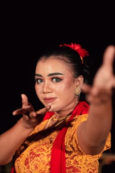 A Balinese woman poses with both her hands in a traditional orange dress and red scarf on her body in the festival