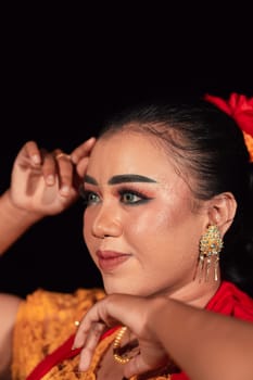 a Sharp gaze from an Indonesian woman with makeup on her face while wearing an orange dress and golden earrings in the night