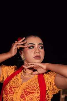 Close-up face of an Indonesian woman with makeup and an orange dress while wearing a piece of gold jewelry on her neck in the night