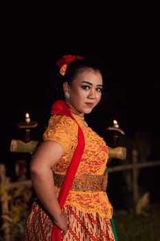 An Asian Traditional dancer in an orange dress with a red scarf and makeup performing at the dance festival in the night
