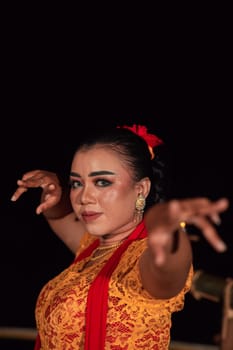 the fierce face of a Balinese woman with makeup in a traditional orange dress and red scarf while dancing at the festival in the night