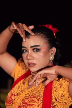 the fierce face of a Balinese woman with makeup in a traditional orange dress and red scarf while dancing at the festival in the night
