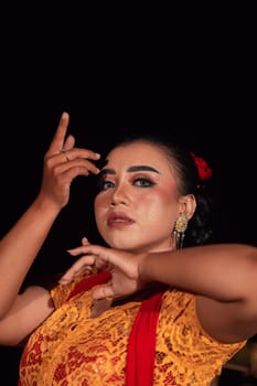 the fierce face of a Balinese woman with makeup in a traditional orange dress and red scarf while dancing at the festival in the night