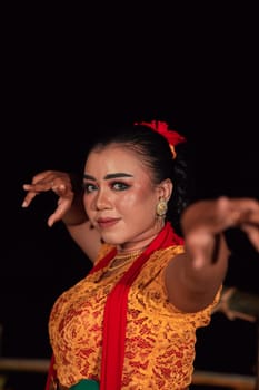 the fierce face of a Balinese woman with makeup in a traditional orange dress and red scarf while dancing at the festival in the night