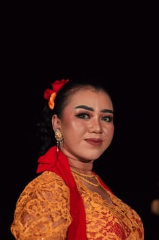 Javanese woman in a traditional orange dress while wearing makeup and a red scarf at a dance festival in Indonesia