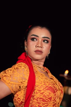 Javanese woman in a traditional orange dress while wearing makeup and a red scarf at a dance festival in Indonesia
