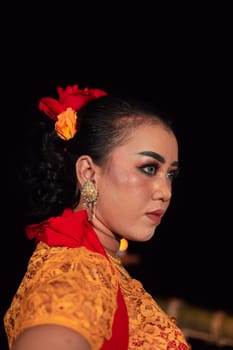 Javanese woman in a traditional orange dress while wearing makeup and a red scarf at a dance festival in Indonesia