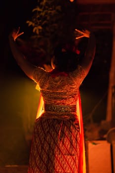A Silhouette body of a Balinese woman in a traditional orange dress while dancing in front of the lighting on the dark night at the festival