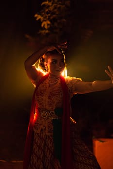 A Silhouette body of a Balinese woman in a traditional orange dress while dancing in front of the lighting on the dark night at the festival