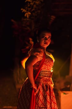 A Silhouette body of a Balinese woman in a traditional orange dress while dancing in front of the lighting on the dark night at the festival