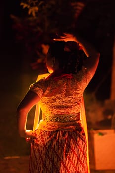 A Silhouette body of a Balinese woman in a traditional orange dress while dancing in front of the lighting on the dark night at the festival