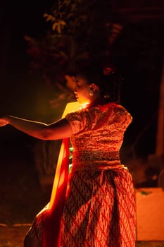A Silhouette body of a Balinese woman in a traditional orange dress while dancing in front of the lighting on the dark night at the festival