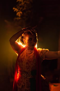 A Silhouette body of a Balinese woman in a traditional orange dress while dancing in front of the lighting on the dark night at the festival