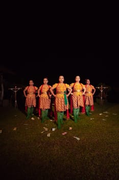 Balinese dancers standing together with red scarf and orange costumes on the stage after performing the traditional dance at the festival