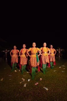 Balinese dancers standing together with red scarf and orange costumes on the stage after performing the traditional dance at the festival