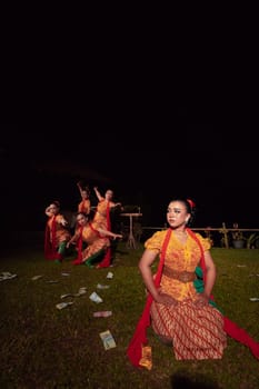 A Group of Indonesian dancers performing on the stage with a red scarf and traditional orange dress inside the festival during the night
