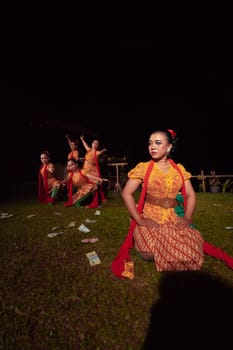 A Group of Indonesian dancers performing on the stage with a red scarf and traditional orange dress inside the festival during the night