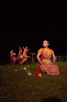 A Group of Indonesian dancers performing on the stage with a red scarf and traditional orange dress inside the festival during the night