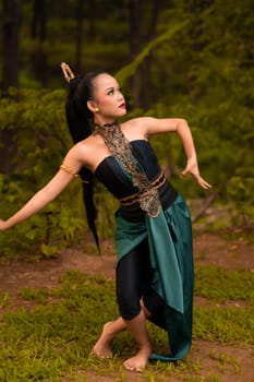 Indonesian woman with long black hair wearing a green costume with makeup in front of the forest during the festival