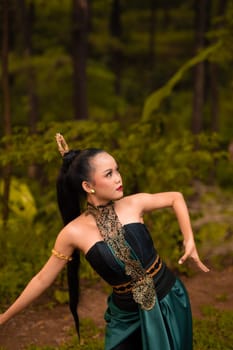 Indonesian woman with long black hair wearing a green costume with makeup in front of the forest during the festival