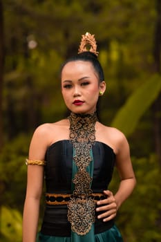 Indonesian woman with the green dress and make-up on her face standing in front of the jungle during the dance festival
