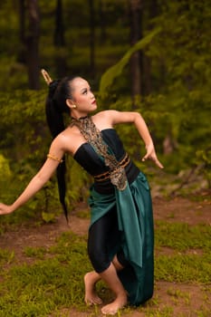 Indonesian woman with long black hair wearing a green costume with makeup in front of the forest during the festival