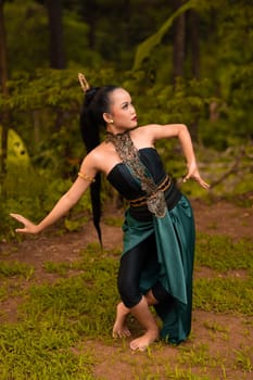 Indonesian woman with long black hair wearing a green costume with makeup in front of the forest during the festival