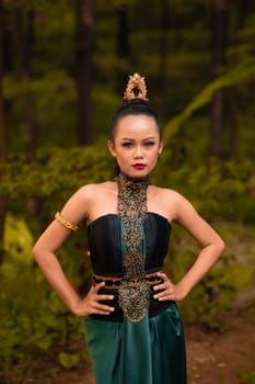 Balinese woman in makeup and gold jewelry on her body with a black costume standing in front of the jungle