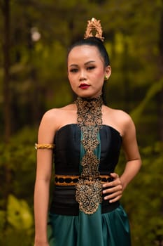 Indonesian woman with the green dress and make-up on her face standing in front of the jungle during the dance festival