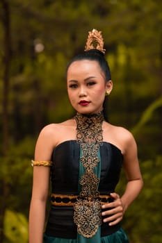Indonesian woman with the green dress and make-up on her face standing in front of the jungle during the dance festival