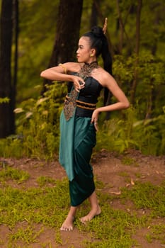 Beautiful Indonesian dancers with traditional green costumes and black tied hair posing inside the forest after performing