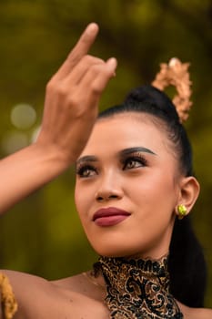 Portrait of a Balinese woman with beautiful makeup and tied black hair on a brave facial expression inside the jungle