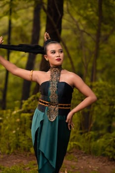 Beautiful Asian woman holding her black hair while standing in front of the forest in a green costume during the festival
