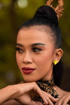 Beautiful Asian woman with makeup and tied black hair wearing a piece of black jewelry before performing dancing on the stage inside the jungle festival
