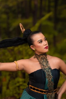 Gorgeous Asian woman in makeup with black hair and red lipstick wearing golden jewelry during the dance performance in front of the jungle
