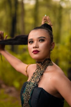 Gorgeous Asian woman in makeup with black hair and red lipstick wearing golden jewelry during the dance performance in front of the jungle