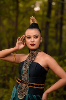 Beautiful Indonesian woman with a green dress and makeup on her face posing in front of the forest with their hand during the morning