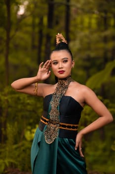 Beautiful Indonesian woman with a green dress and makeup on her face posing in front of the forest with their hand during the morning
