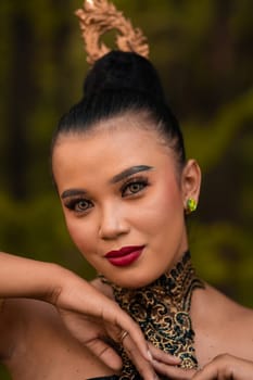 Beautiful eyes of an Asian woman in makeup and red lipstick while wearing gold jewelry and black hair while standing in front of the jungle
