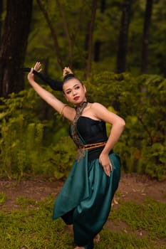 Asian woman holding her black hair in a green costume while wearing makeup and posing in front of the forest during the dance festival inside the village